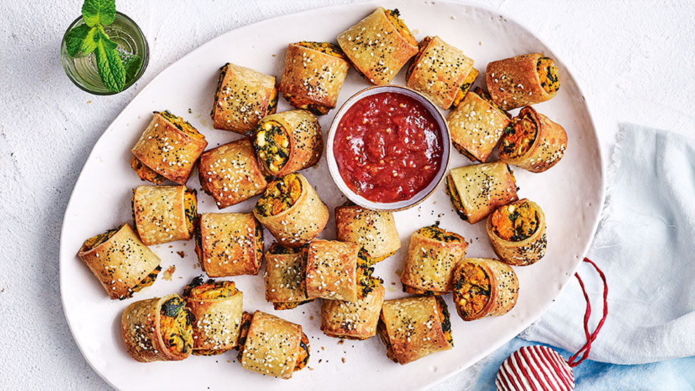 Gluten-free sweet potato and fetta sausage rolls on a serving platter with tomato sauce in the middle